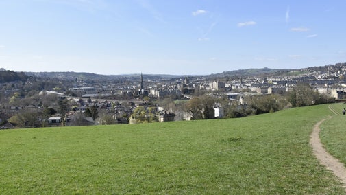 View of the grass at Bathwick Fields with Bath city centre beyond, bright blue skies.